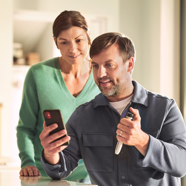 A middle-aged man and woman sit on their couch; the woman holds a smartphone while the man looks at a Tempo Pen with Tempo Smart Button attached.