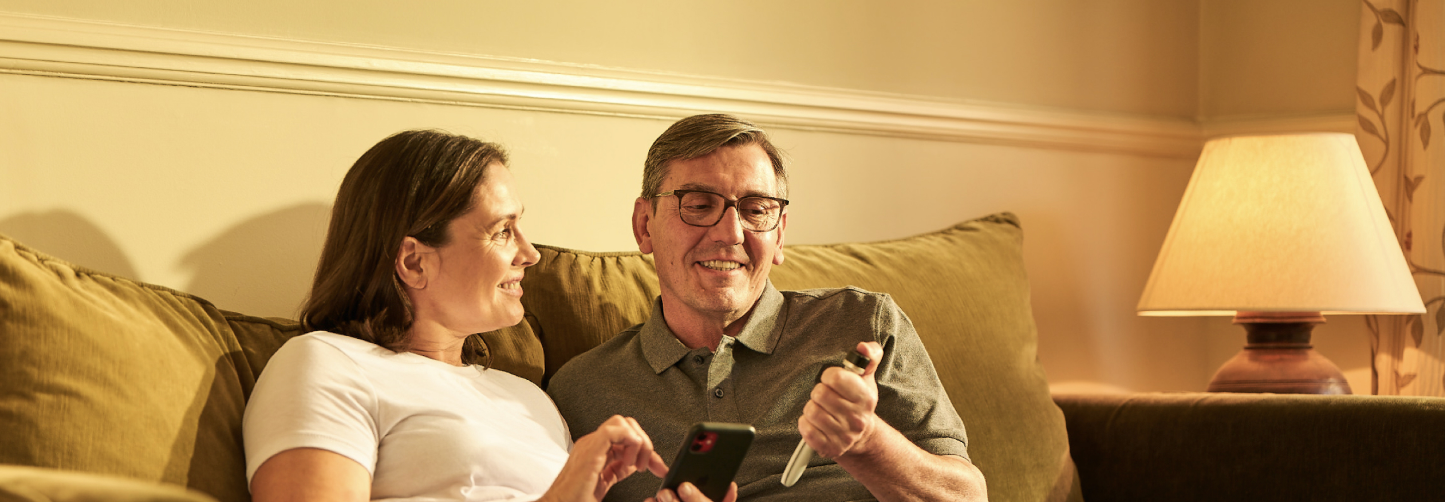 A man and a woman sit together. She holds a phone while smiling at him. He is smiling back while pressing a Tempo Smart Button on his Tempo Pen.